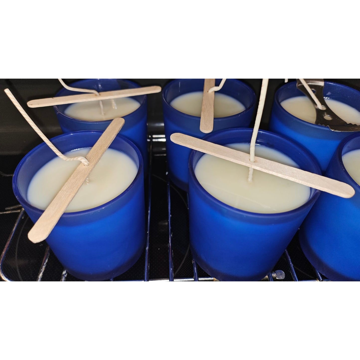 Blue cups with white liquid and wooden sticks inside, placed on a metal rack.