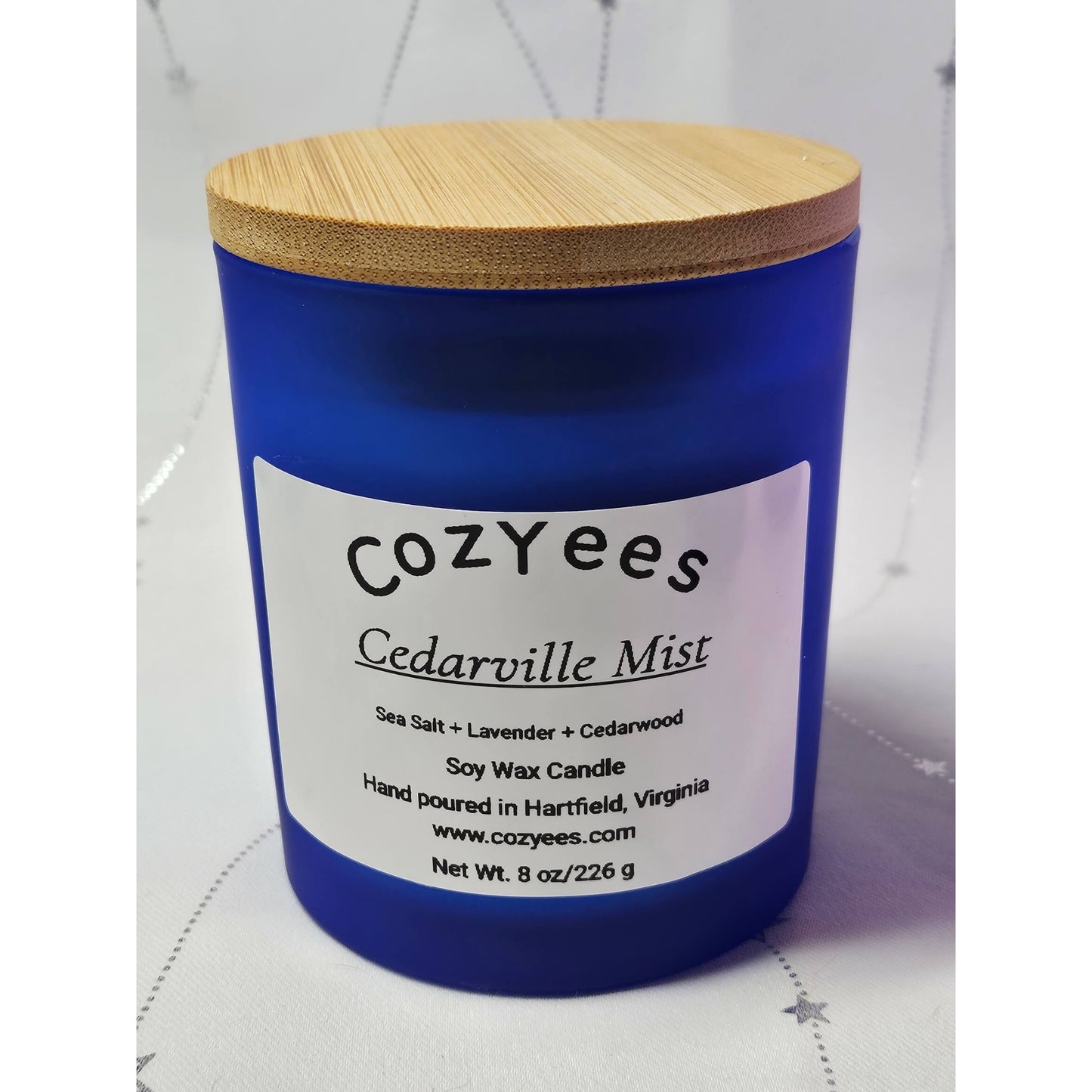 Blue candle with a wooden lid labeled 'cozYees Cedarville Mist' on a white background.