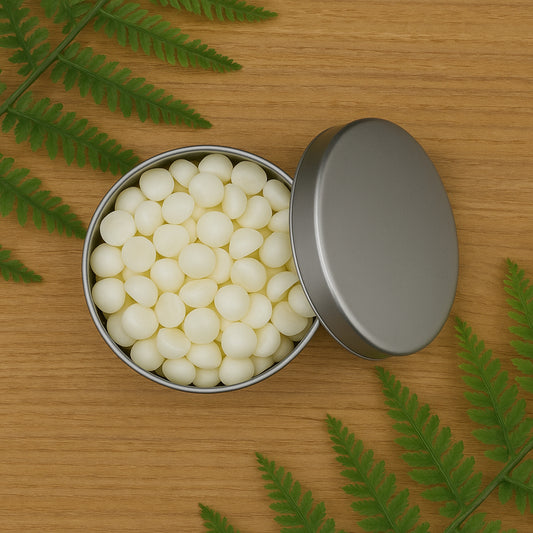 Cozyees wax dots in silver tin on wood table with greenery.