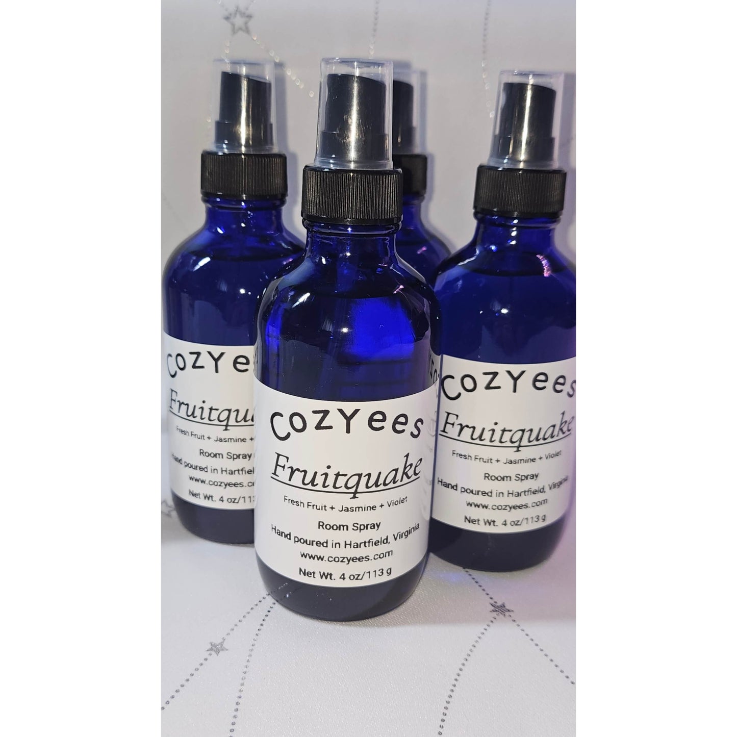 Three Cozyees Fruitquake room spray bottles on a white surface.