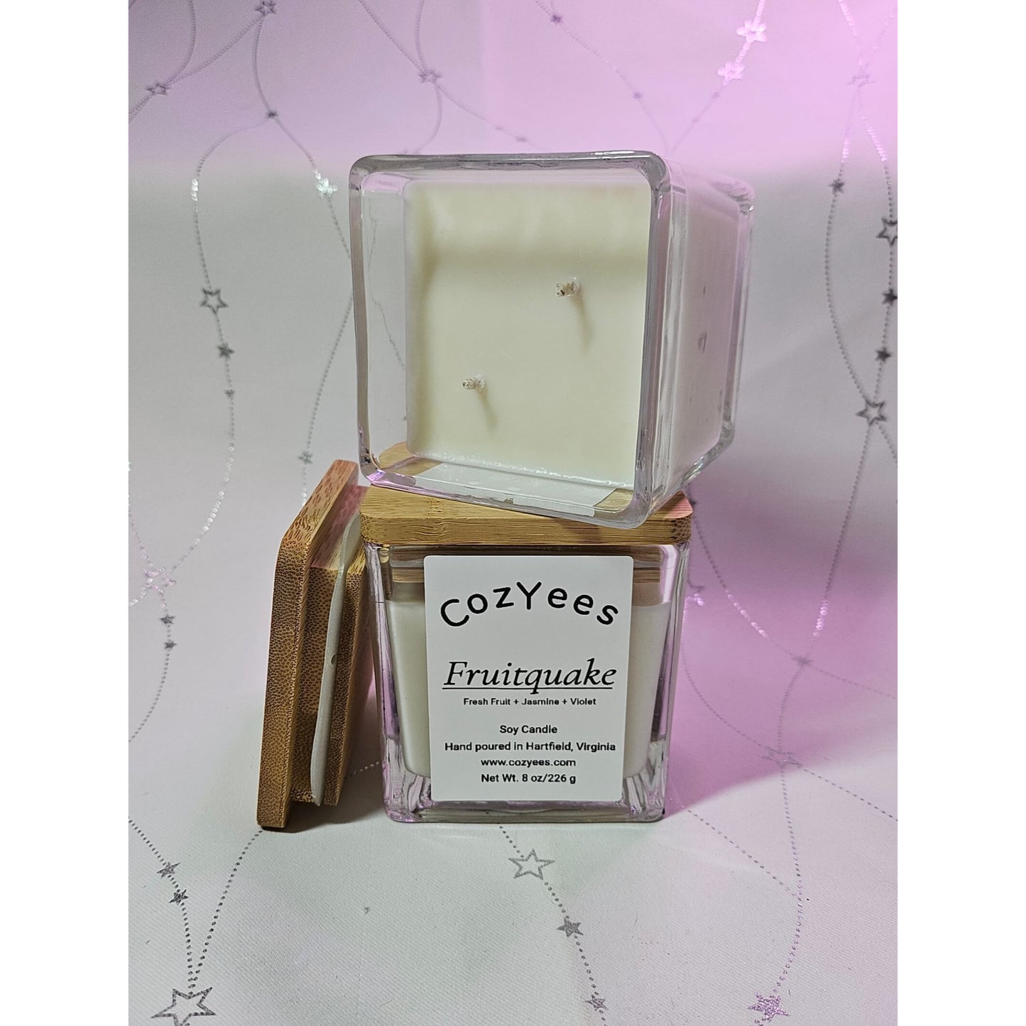 Cozyees Fruitquake candle in a clear box on a decorative background