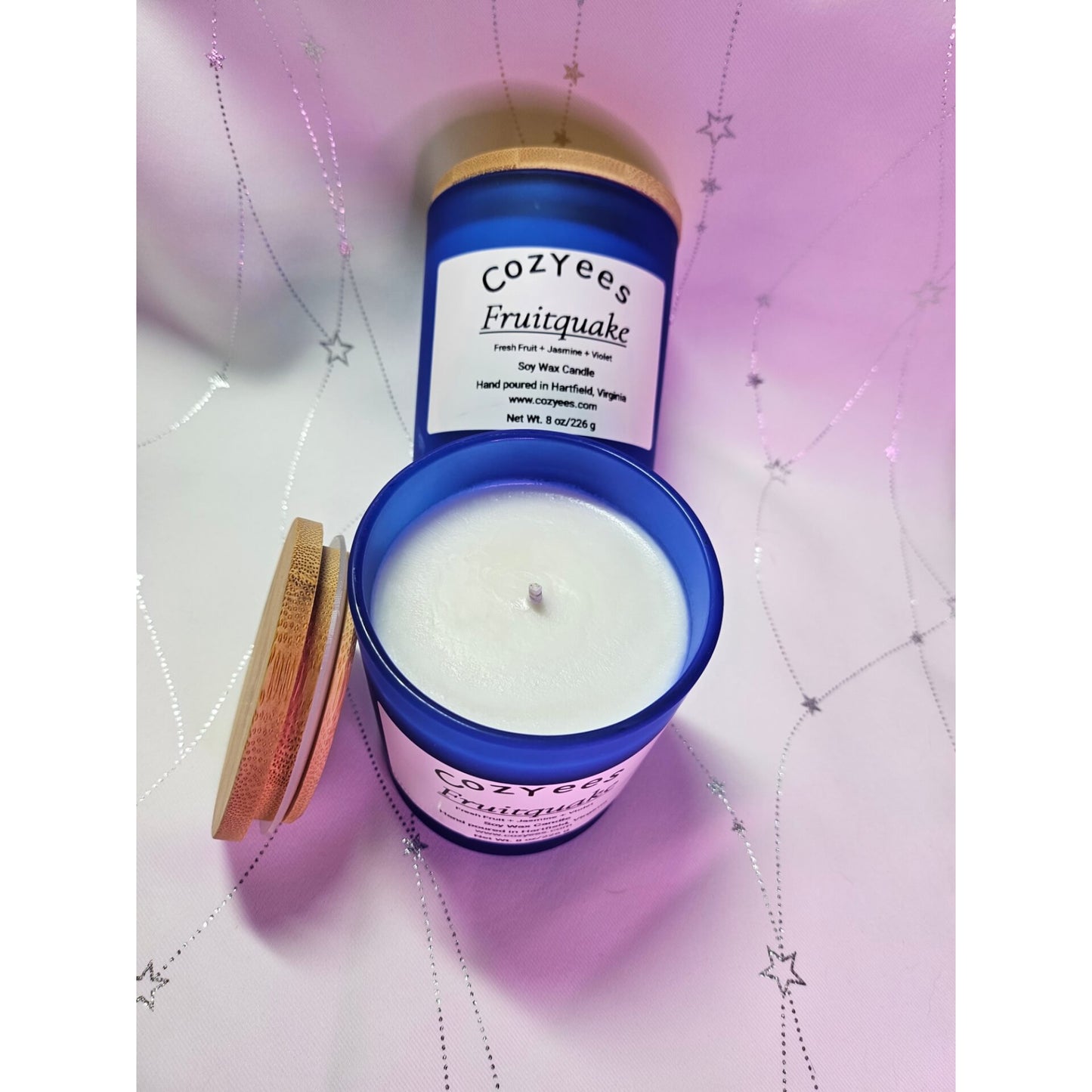 Cozyees Fruitquake candle with blue container on a pink textured background