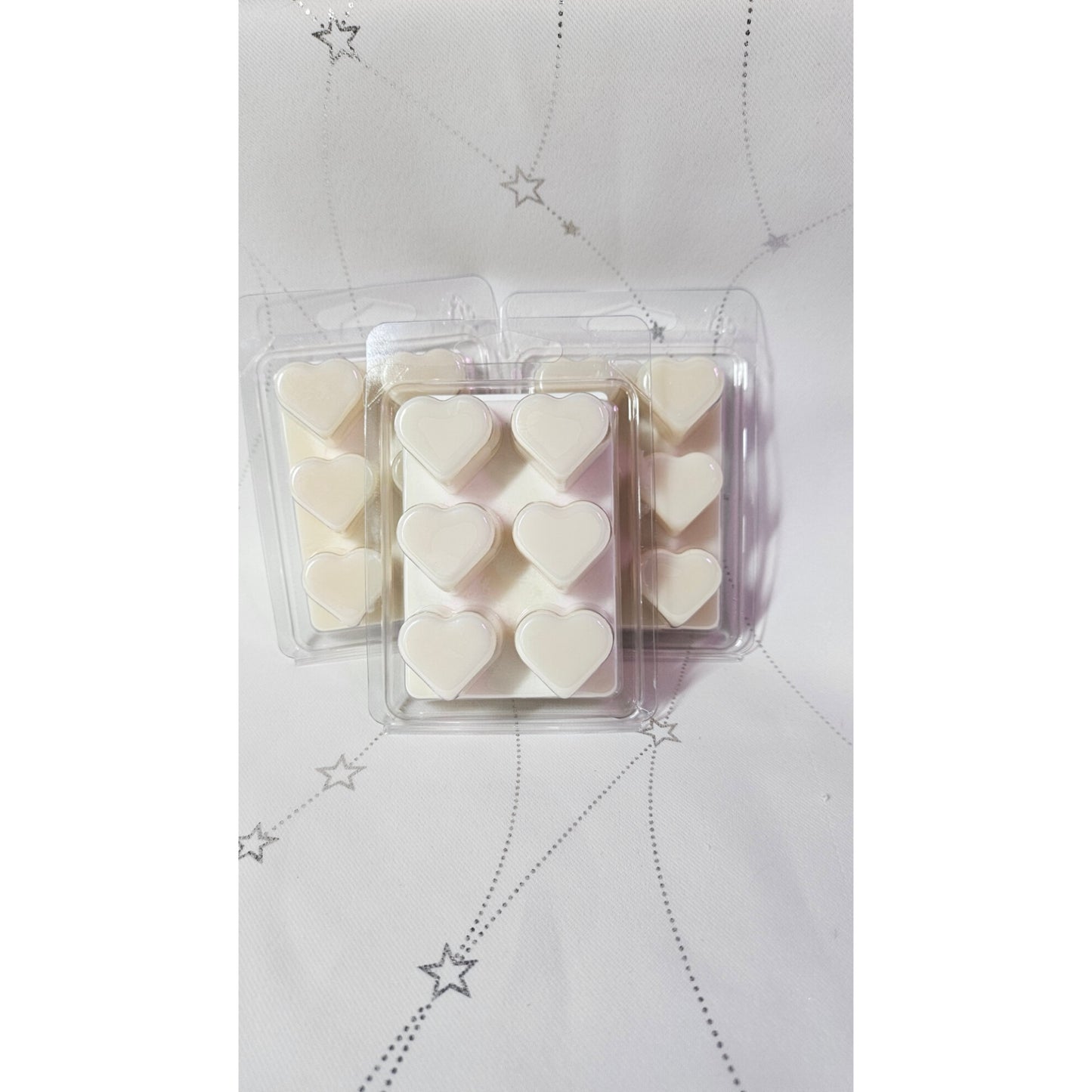 Heart-shaped wax melts in a clear plastic packaging on a light gray background with star patterns.