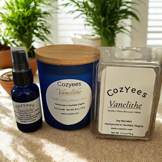 Cozyees Vanelithe candle, spray bottle, and wax melt packaging on a surface with plants in the background.