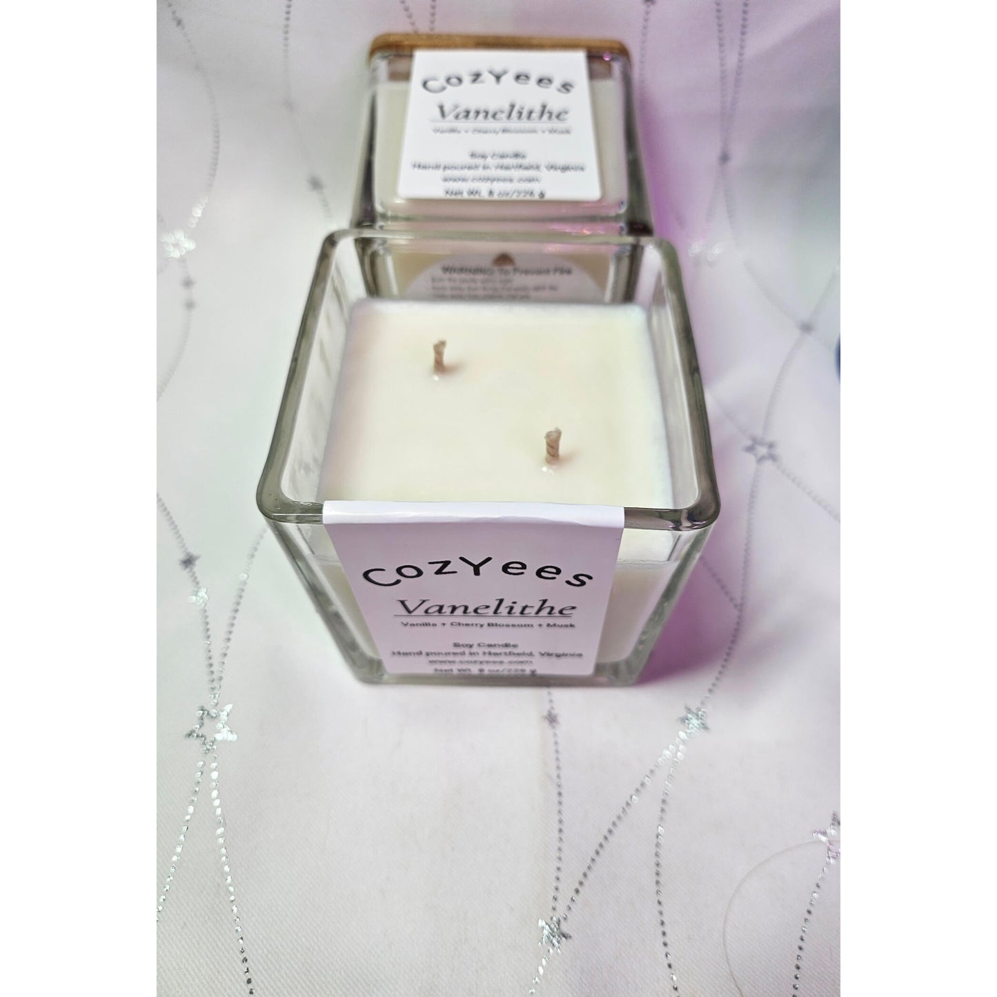 Cozyees Vanelithe candle in a glass container on a textured surface