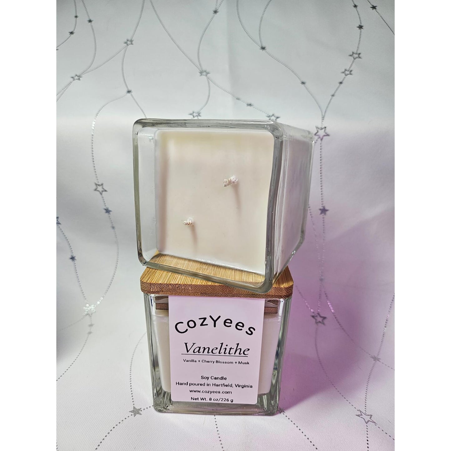 Square glass candle with wooden base and CozYees label on a decorative background