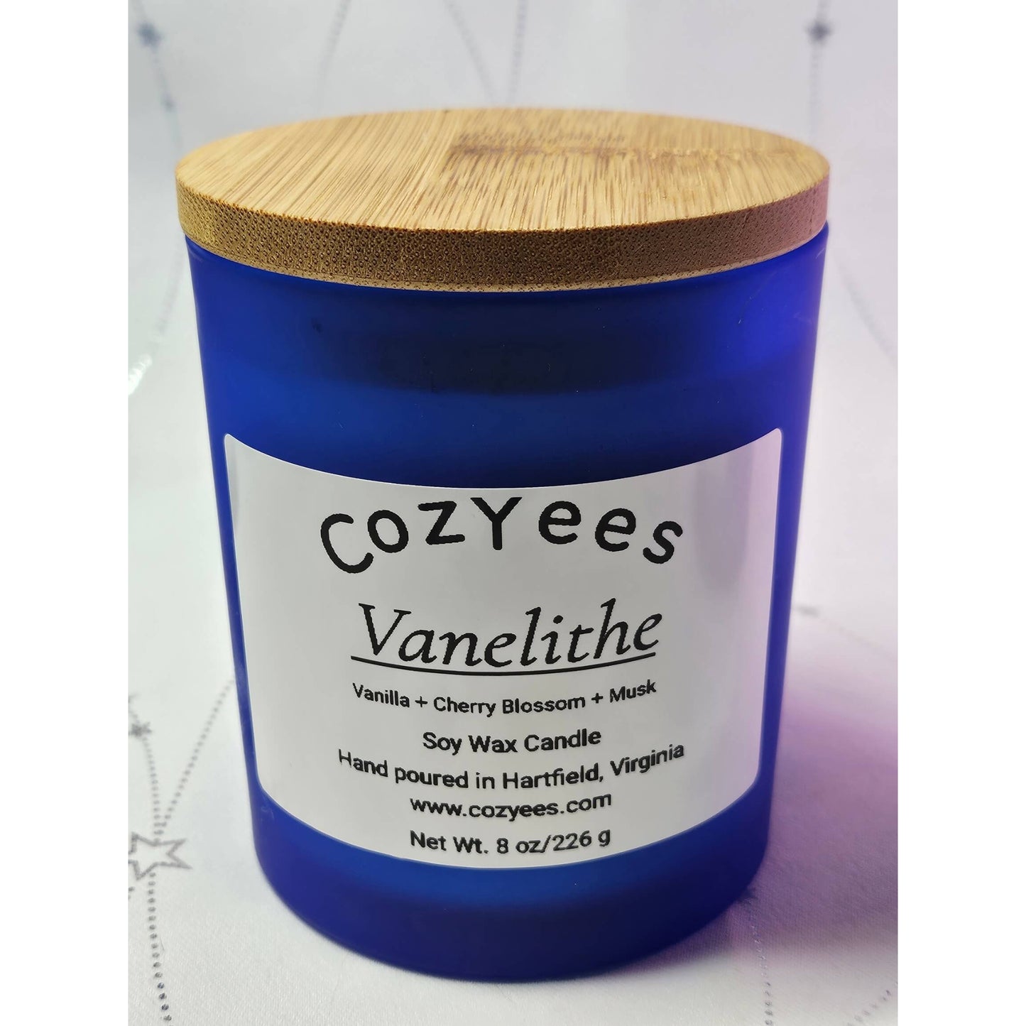 Blue candle with a wooden lid labeled 'Cozyees Vanelithe' on a white background.