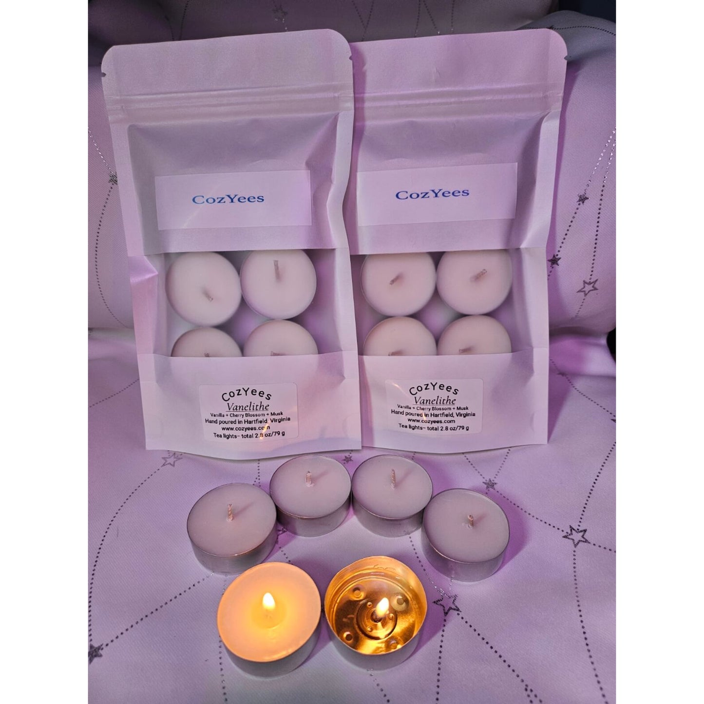 CozYees candles in packaging on a purple surface with two lit candles.