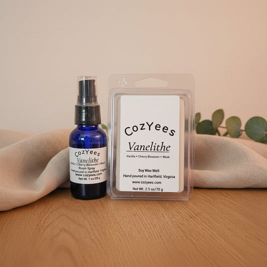 Cozyees Vanelithe soy wax melt set featuring a small blue spray bottle and a clear clamshell wax melt package on a wooden surface against a dark background.