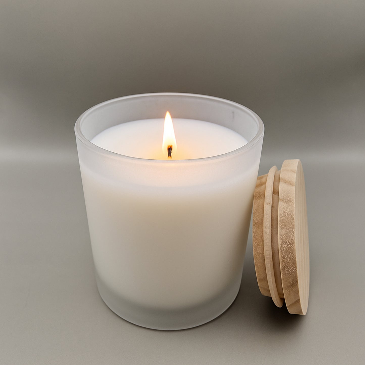 White candle in a glass jar with a wooden lid on a neutral background