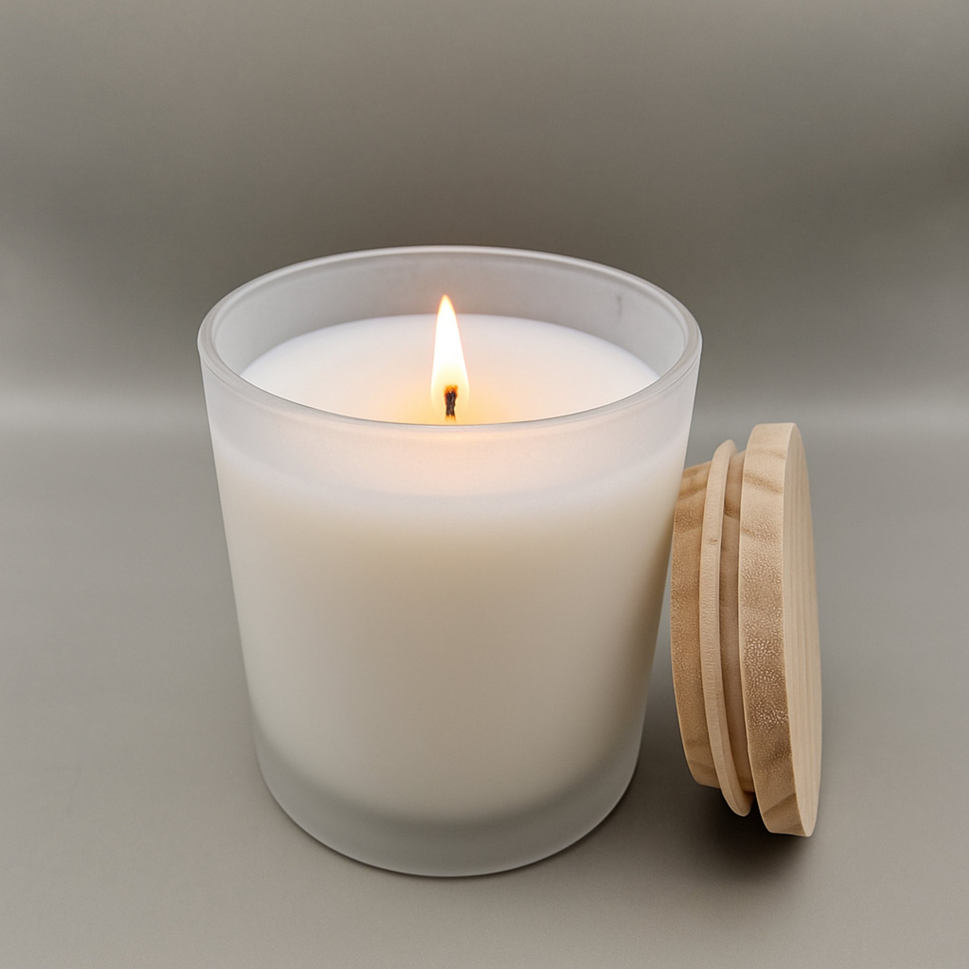 White candle in a glass jar with a wooden lid on a neutral background