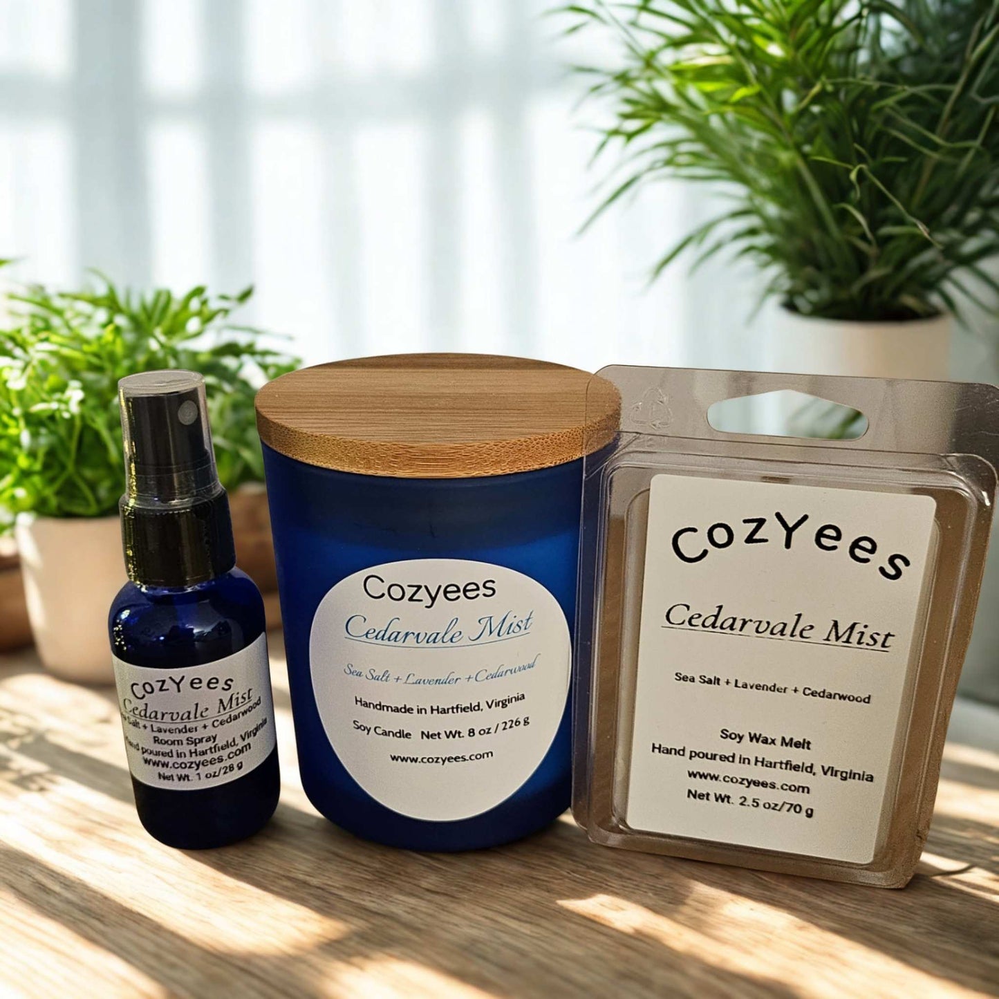 Cozyees Cedarvale Mist candle, spray bottle, and wax melt on a wooden surface with plants in the background.