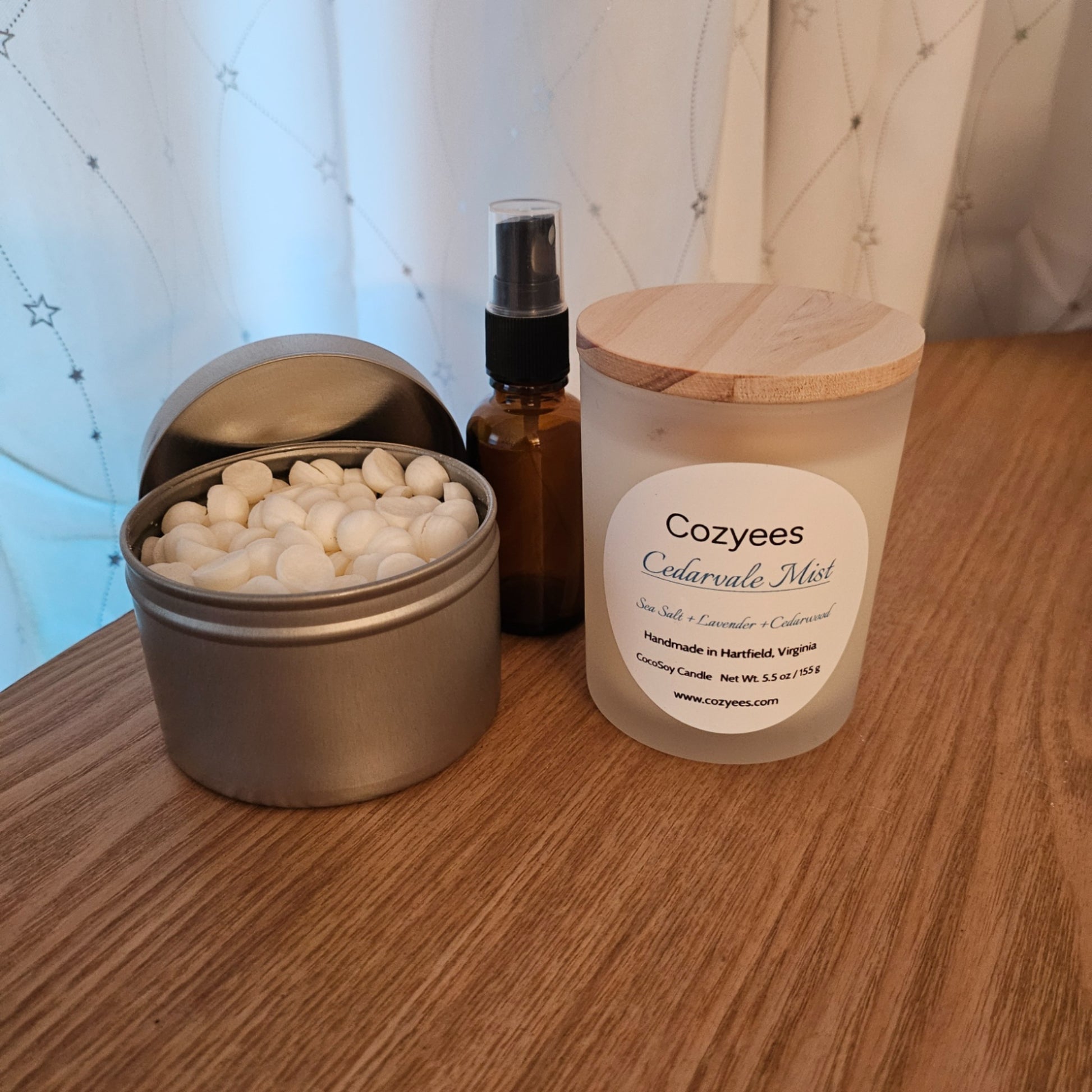 Candle, essential oil bottle, and metal container on a wooden surface with a blurred background