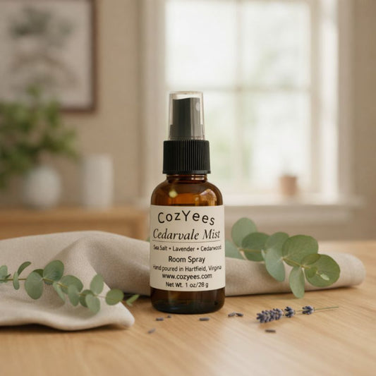Cozyees Cedarvale Miss room spray bottle on a wooden surface with eucalyptus leaves and lavender flowers.