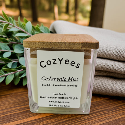 Cozyes Cedarvale Mist candle with a wooden lid on a wooden surface with plants and fabric in the background.