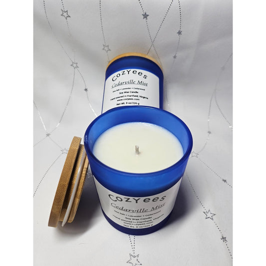 Cozyees Cedarville Mist candle with blue lid on a white textured background