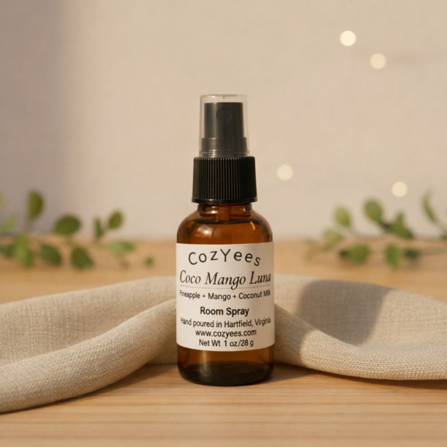 Cozyees Coco Mango Luna room spray bottle on a wooden surface with a blurred background
