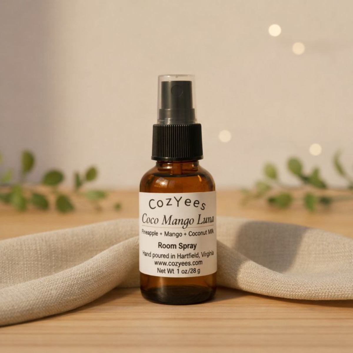 Cozyees Coco Mango Luna room spray bottle on a wooden surface with a blurred background