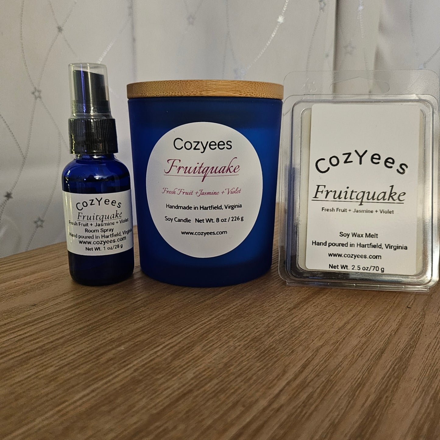 Cozyees Fruityquake product set including a bottle, candle, and wax melt on a wooden surface.