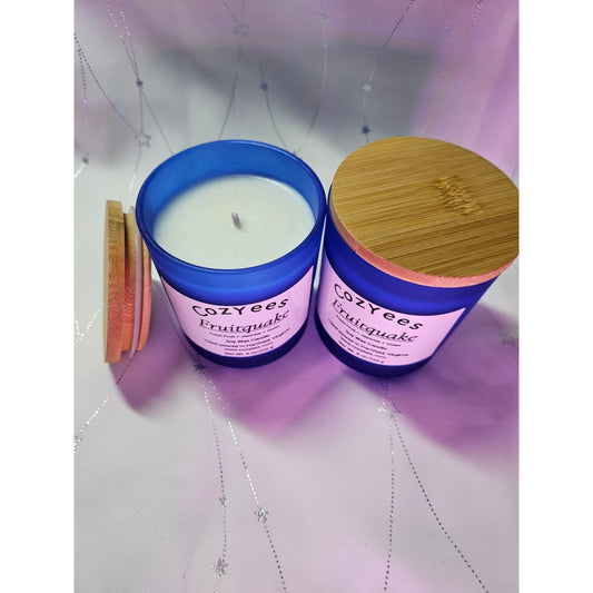 Two Cozyees Fruitcake candles with blue containers and wooden lids on a light purple background.