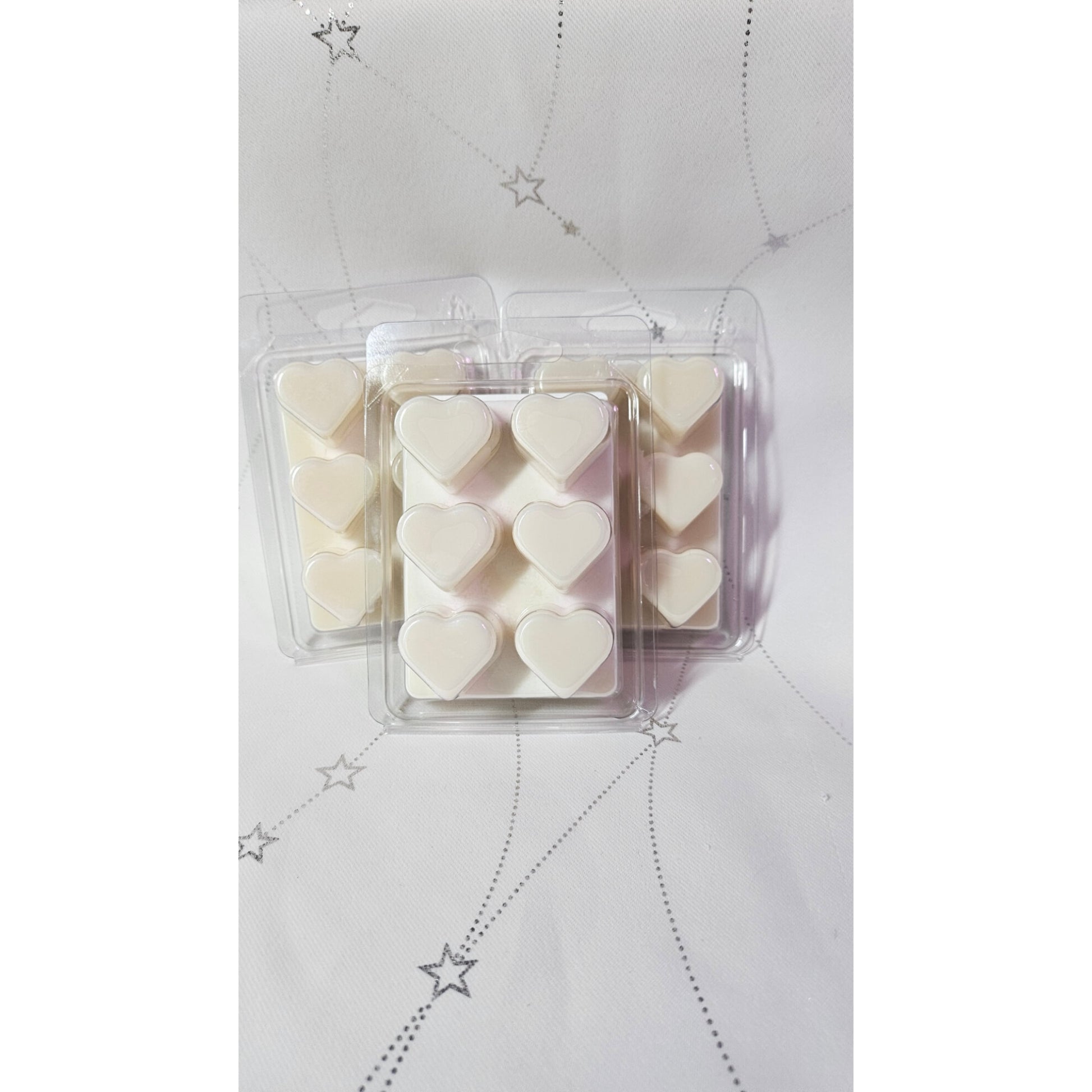 Heart-shaped wax melts in a clear plastic packaging on a light gray background with star patterns.