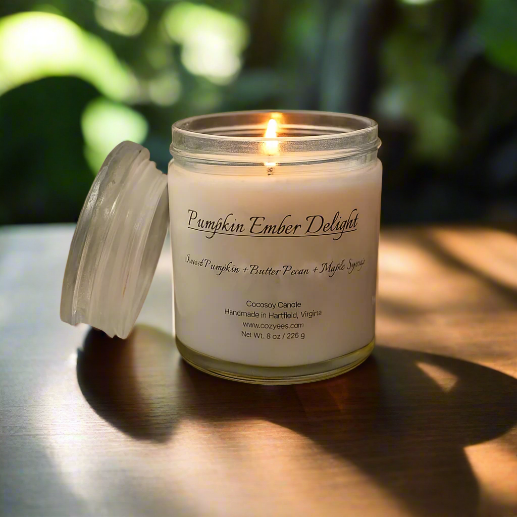 Candle labeled 'Pumpkin Ember Delight' surrounded by pumpkins, pecans, and cinnamon sticks on a wooden surface.