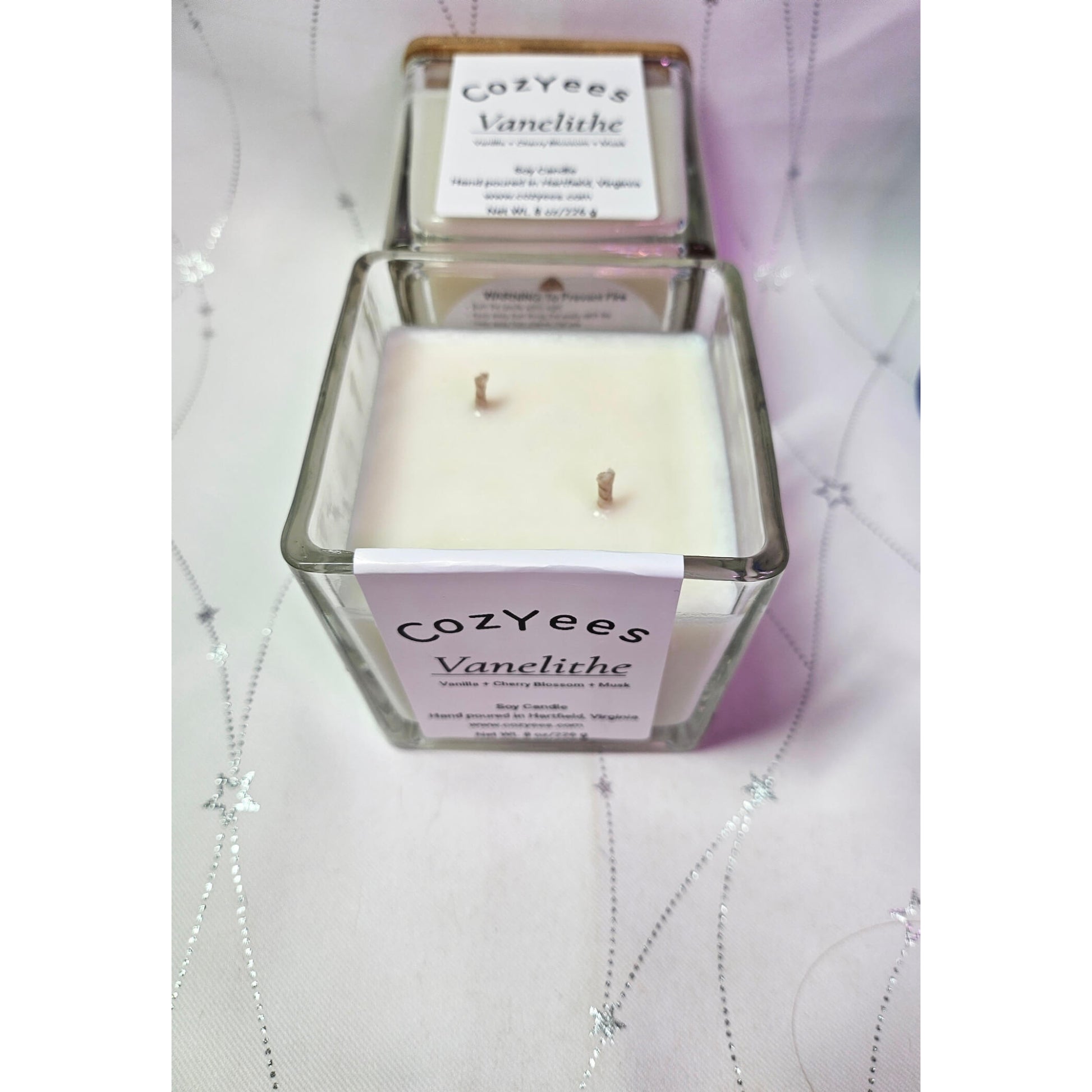 Cozyees Vanelithe candle in a glass container on a textured surface