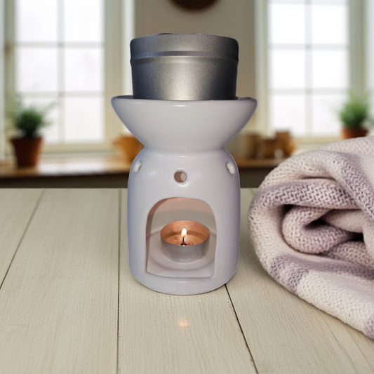 White wax warmer with a lit candle on a wooden surface, with a blurred indoor background.