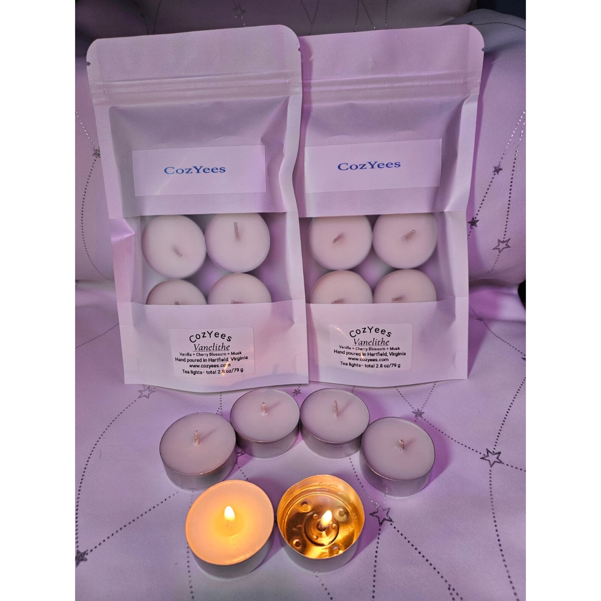 CozYees candles in packaging on a purple surface with two lit candles.