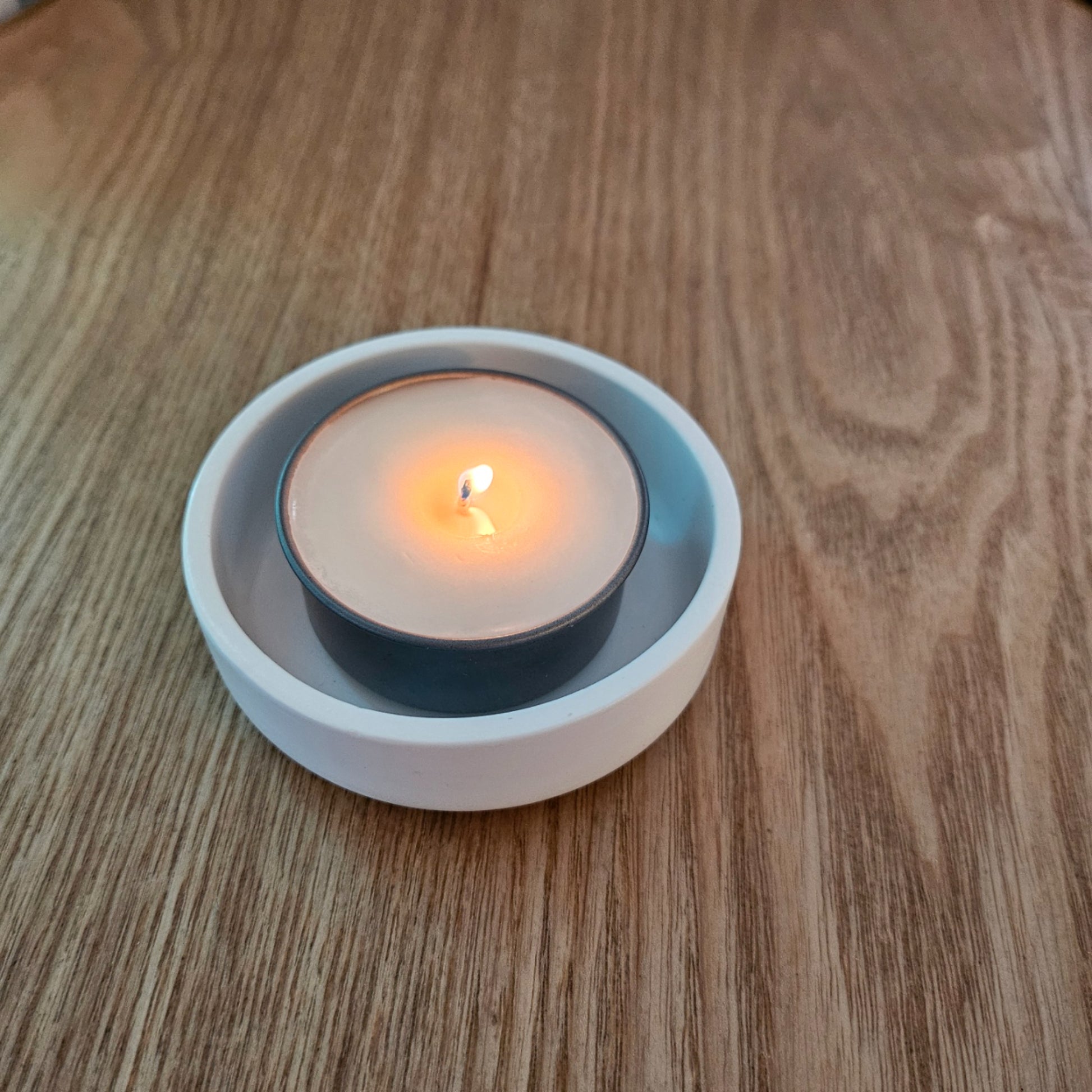 Tealight candle in a white holder on a wooden surface