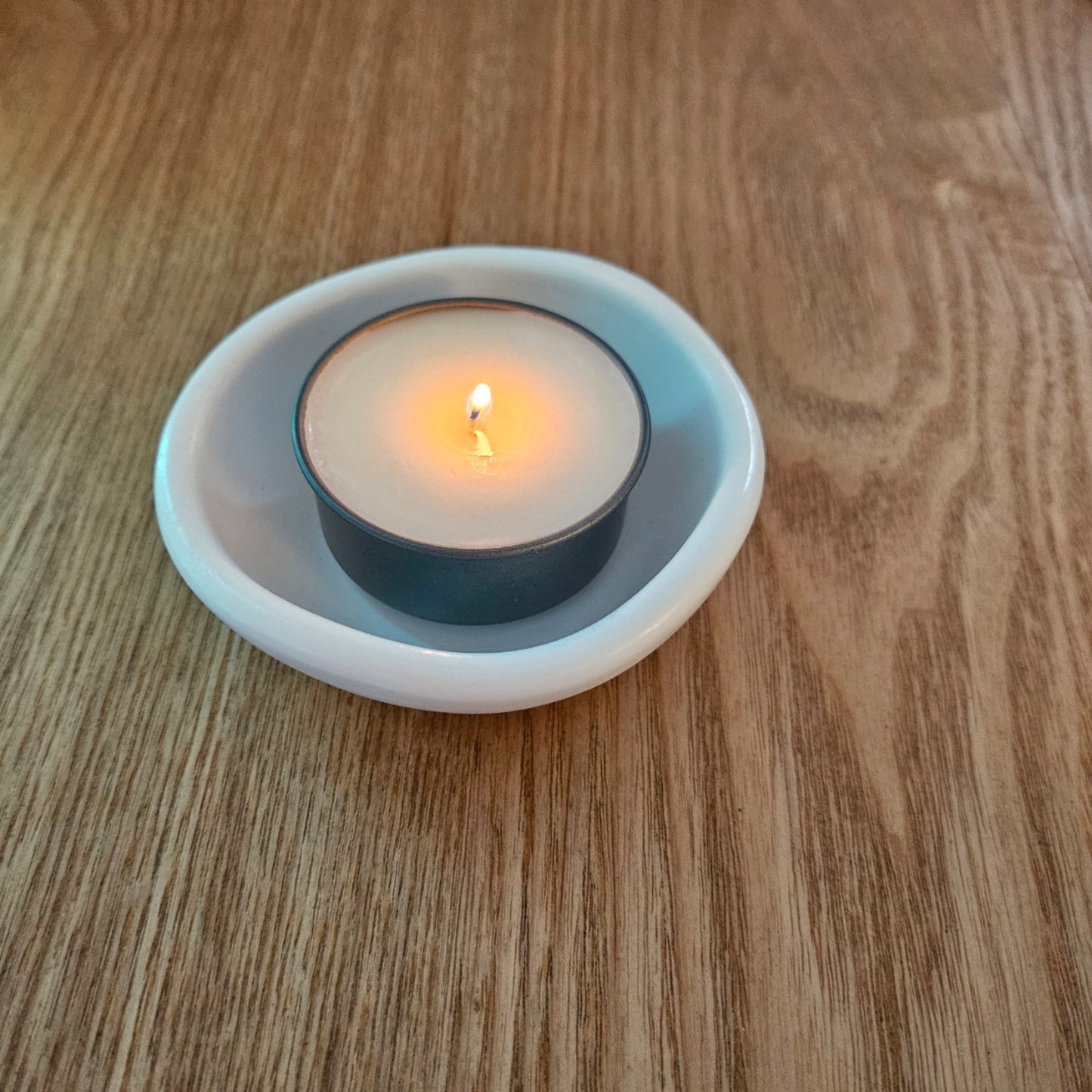 Tea light candle in a white holder on a wooden surface