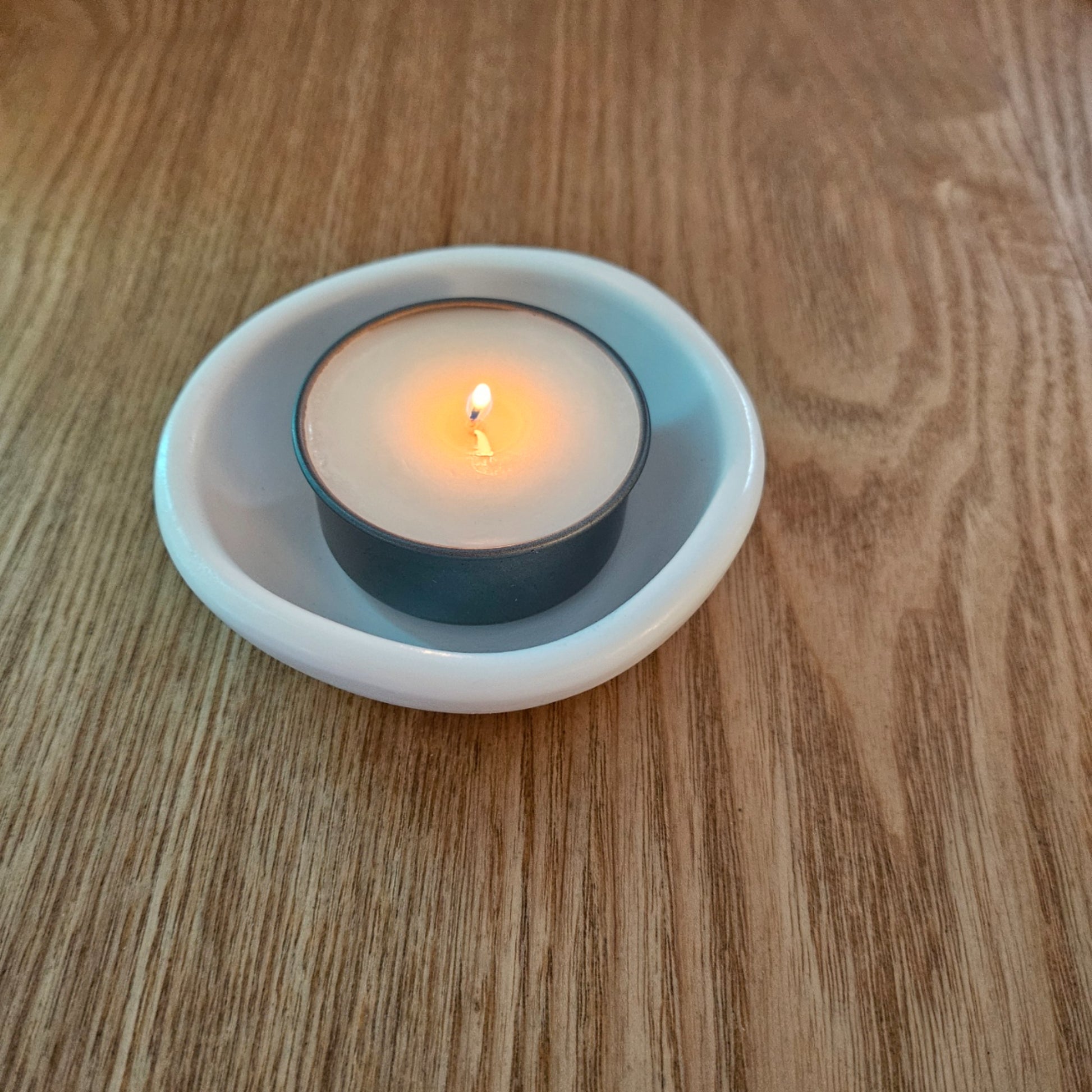 Tea light candle in a white holder on a wooden surface