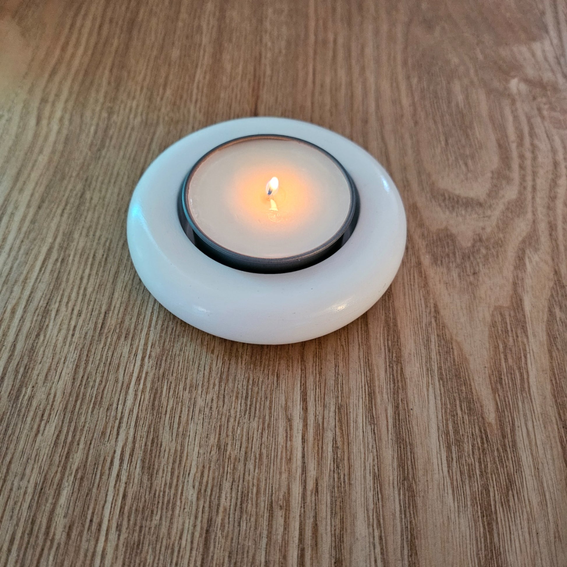 Candle in a white holder on a wooden surface